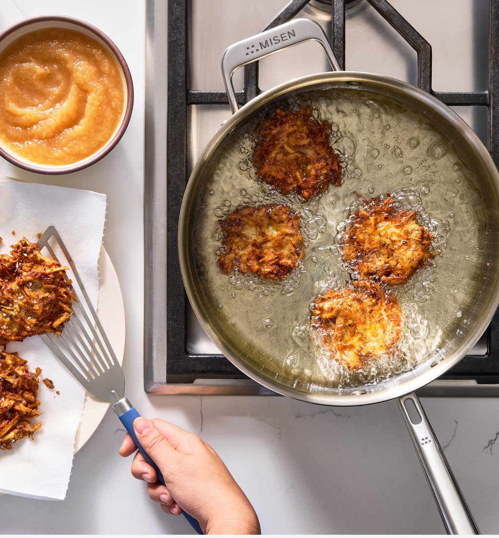 Potato latkes frying in Misen stainless steel pan with applesauce on the side